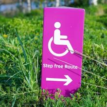 Purple disability placard in grass shows outline of person in wheelchair 