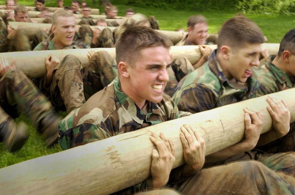 men in military uniforms holding logs to exercise